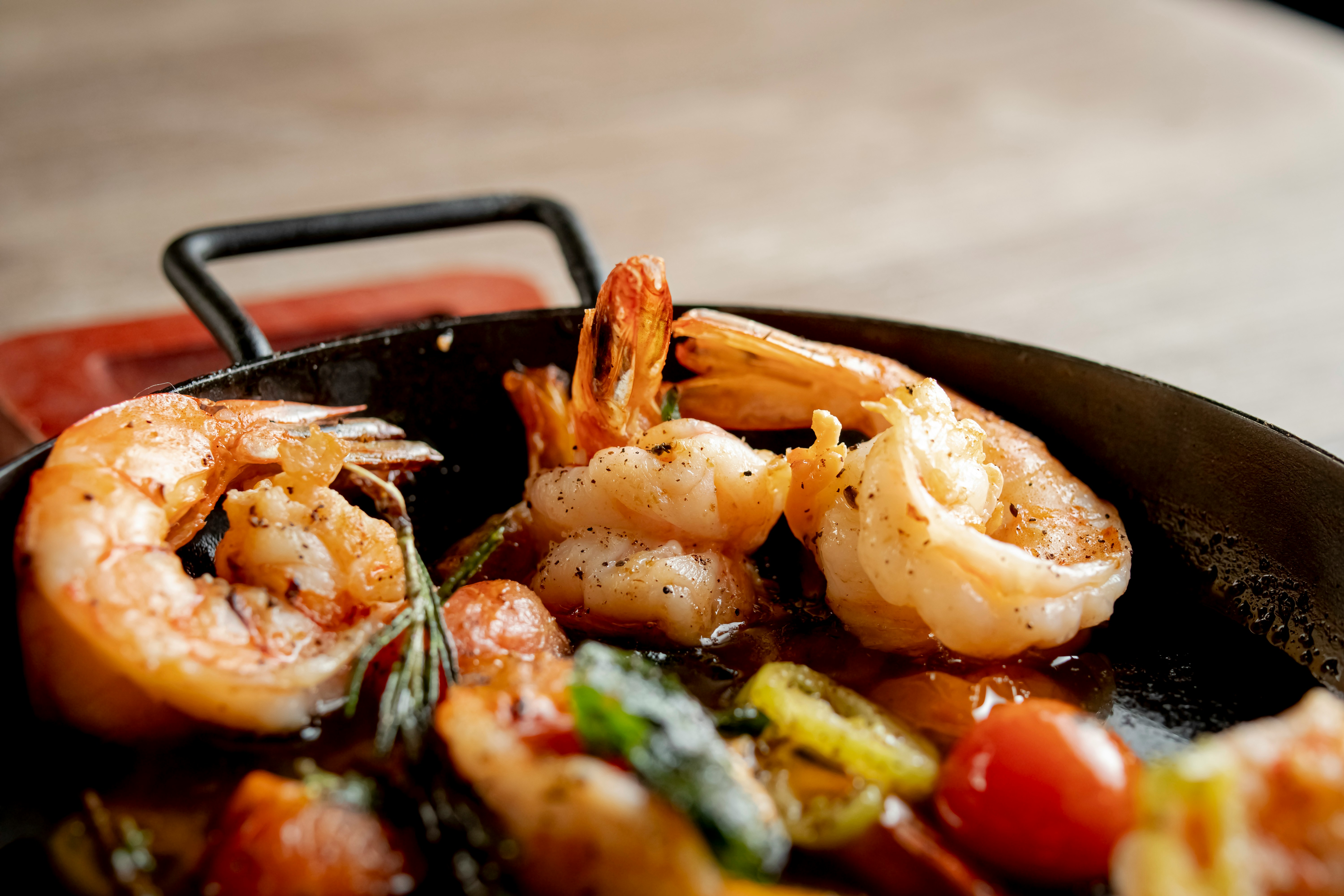 Close-up of cooked prawns, cherry tomatoes, and herbs sizzling in a small black frying pan