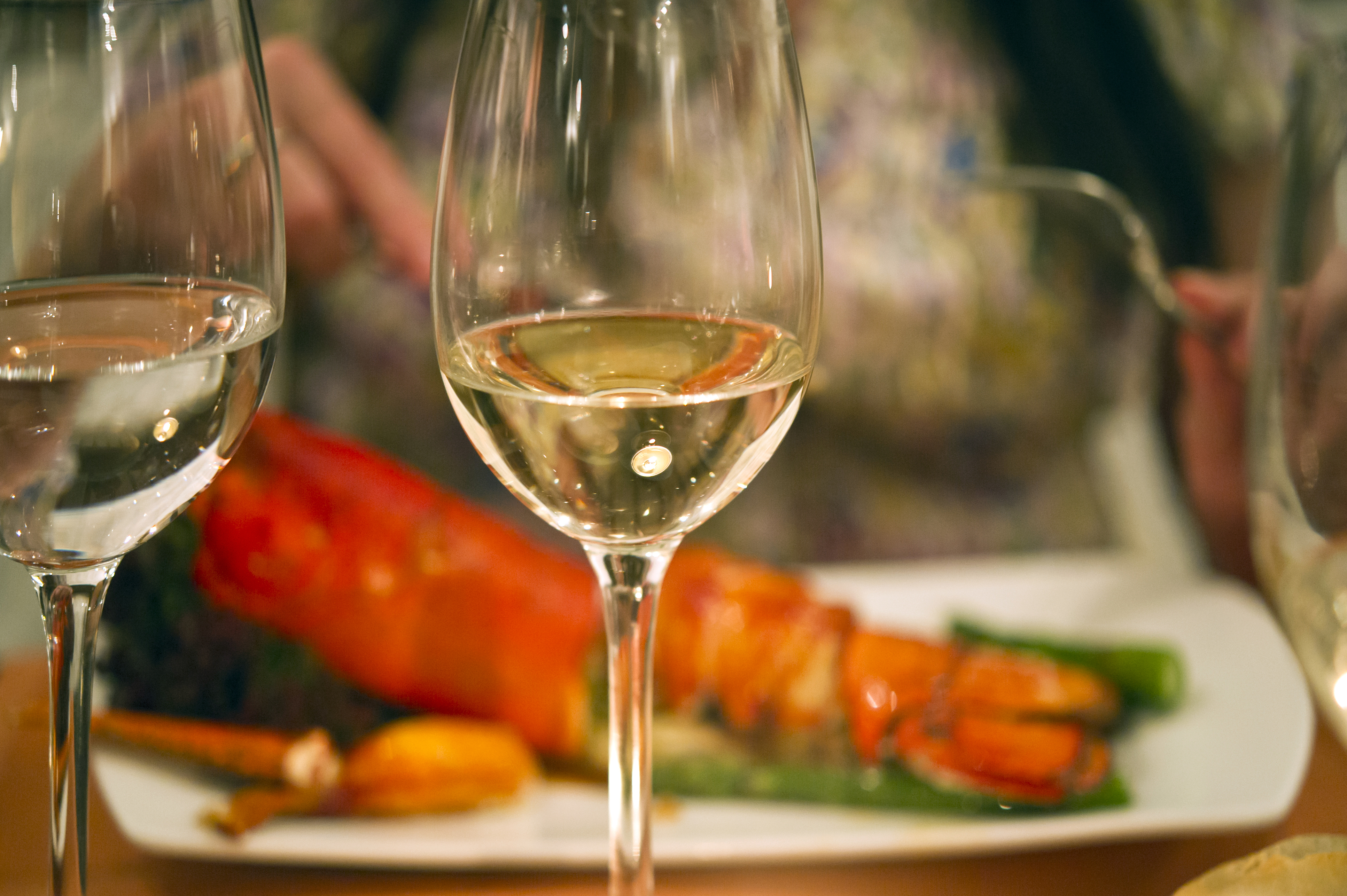 Close-up of wine glasses filled with white wine placed on a restaurant table with a lobster dish.