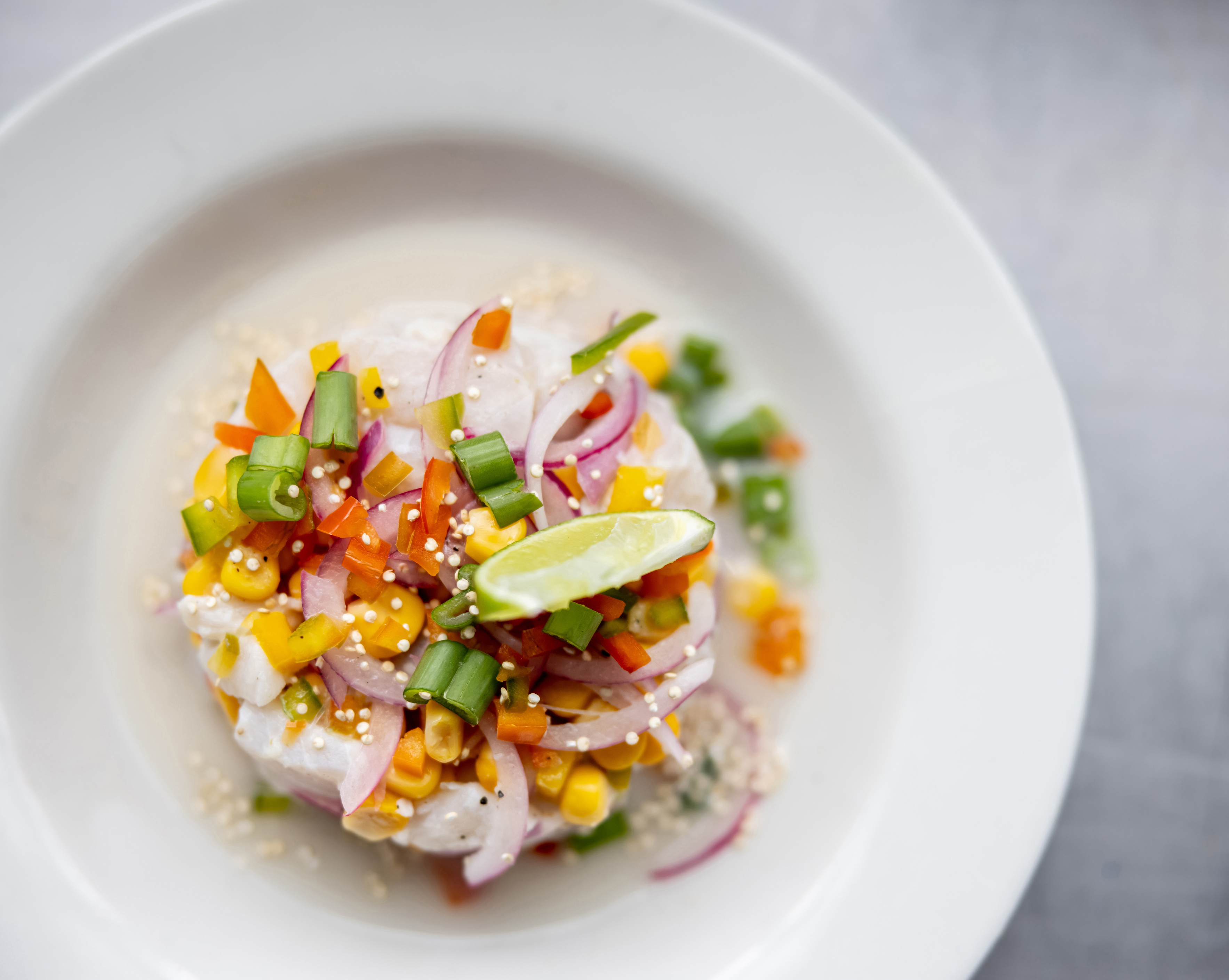 Top-down view of a fresh ceviche dish garnished with red onion, sweetcorn, herbs, and lime wedge