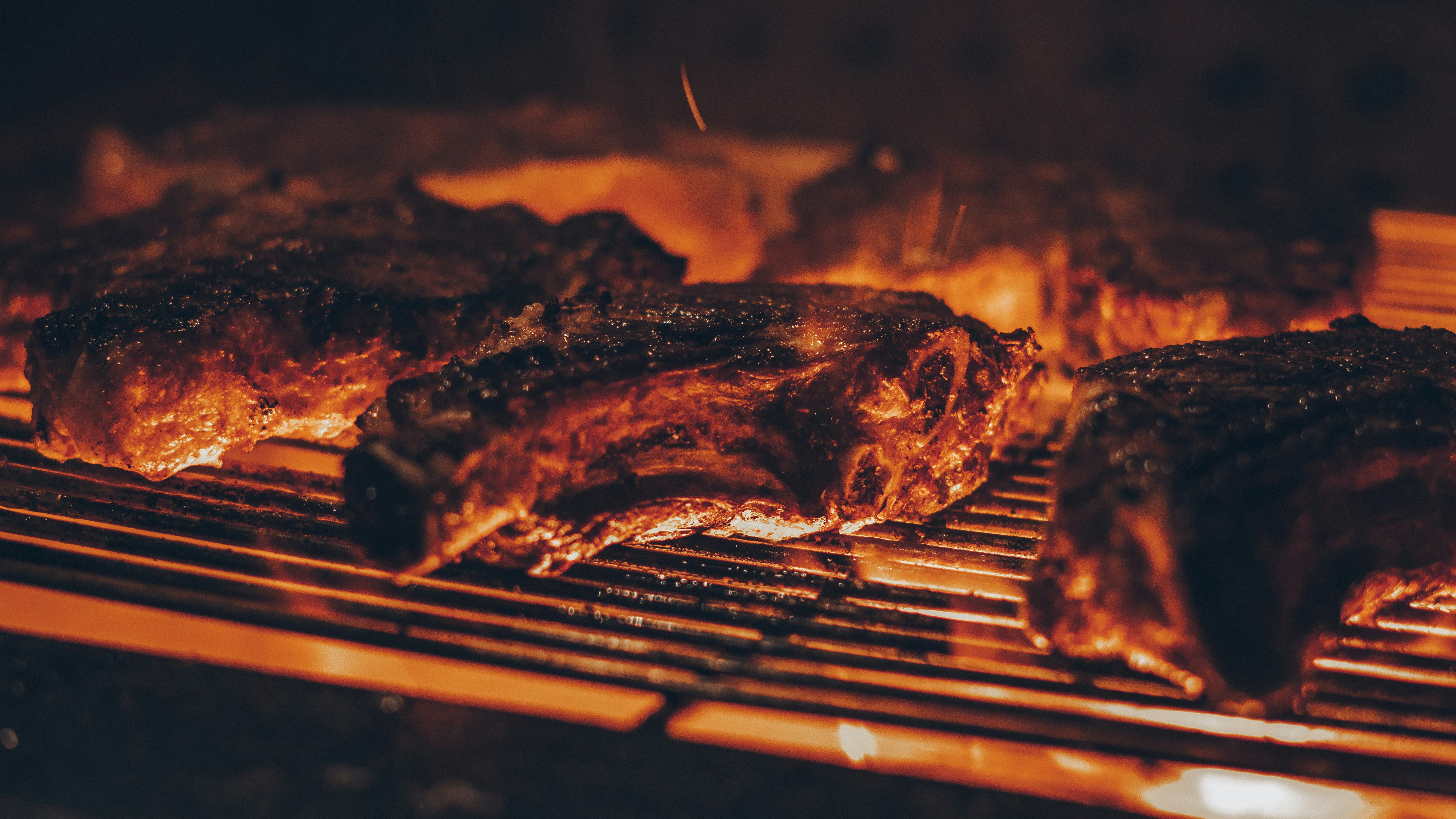 Several thick cuts of meat cooking on hot metal barbecue