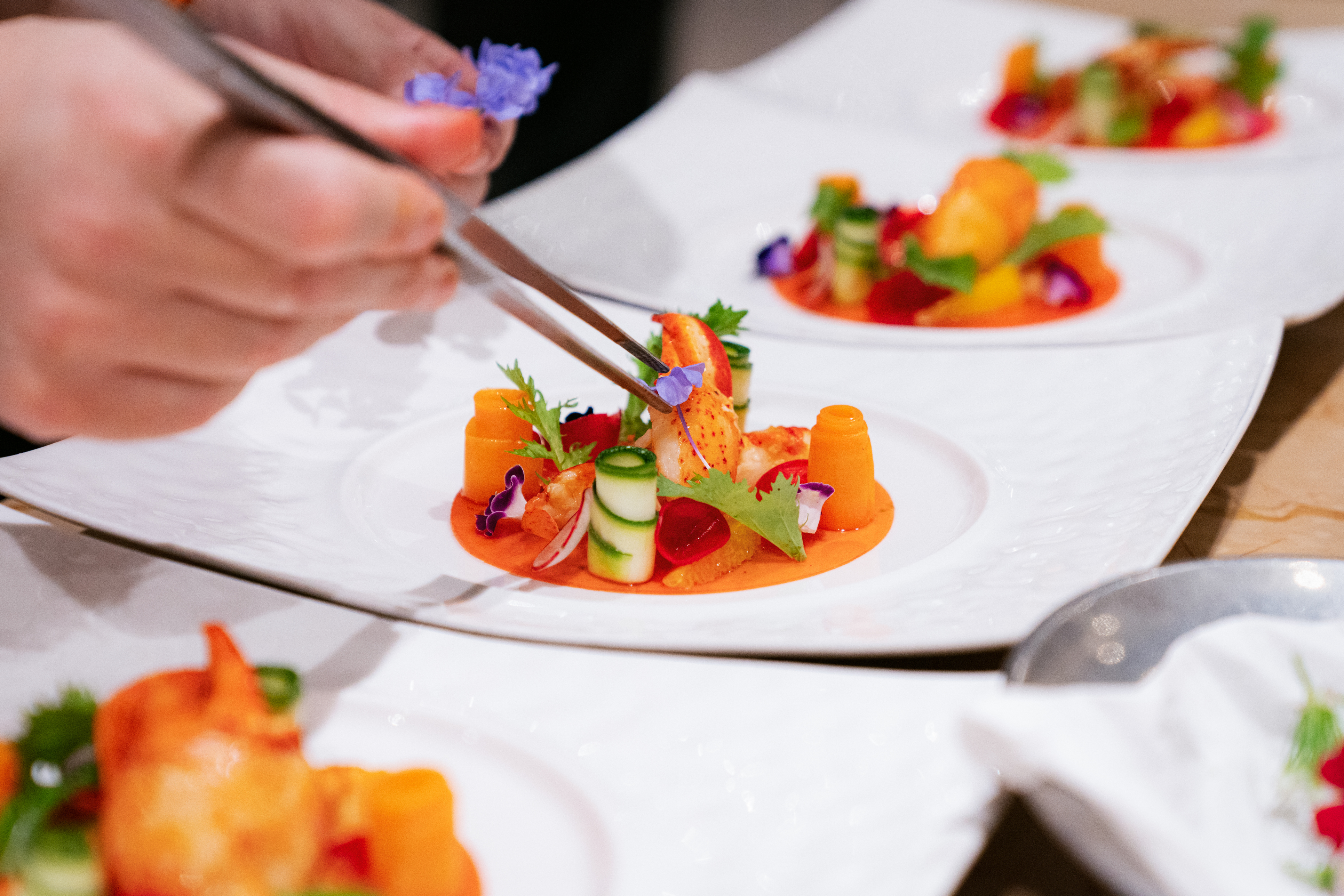 Chef plating fine dining dish with edible flowers and lobster