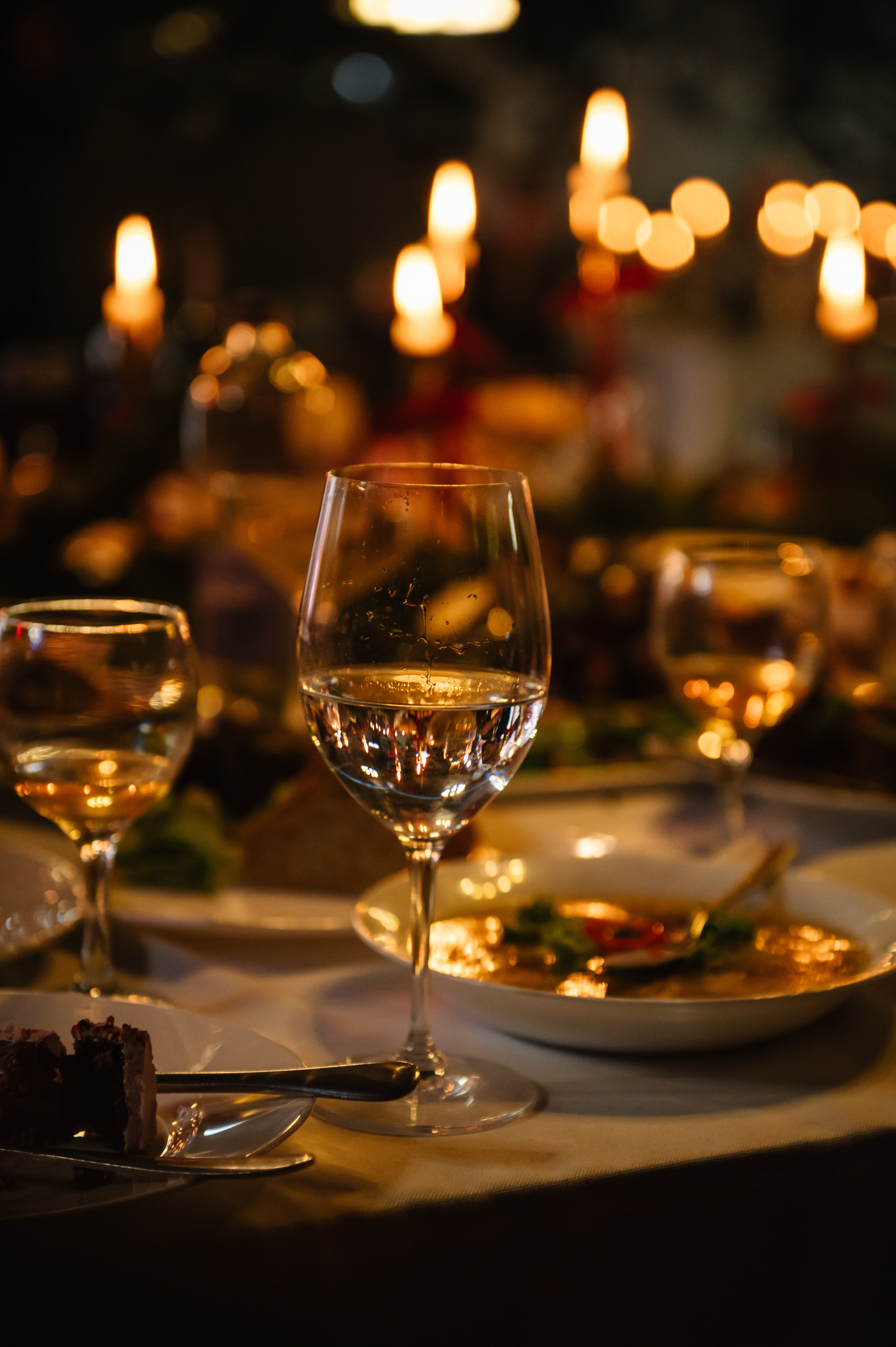 A table set for a formal dinner featuring wine glasses, plates of food, and glowing candlelight in the background